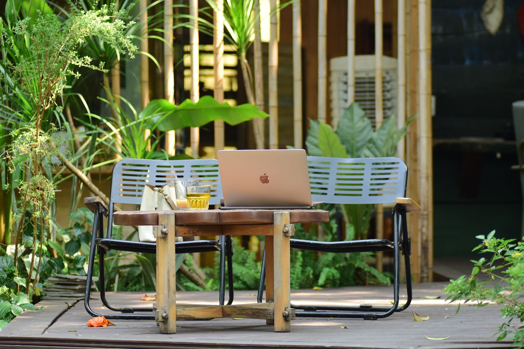 A laptop open on a wooden table in a garden courtyard